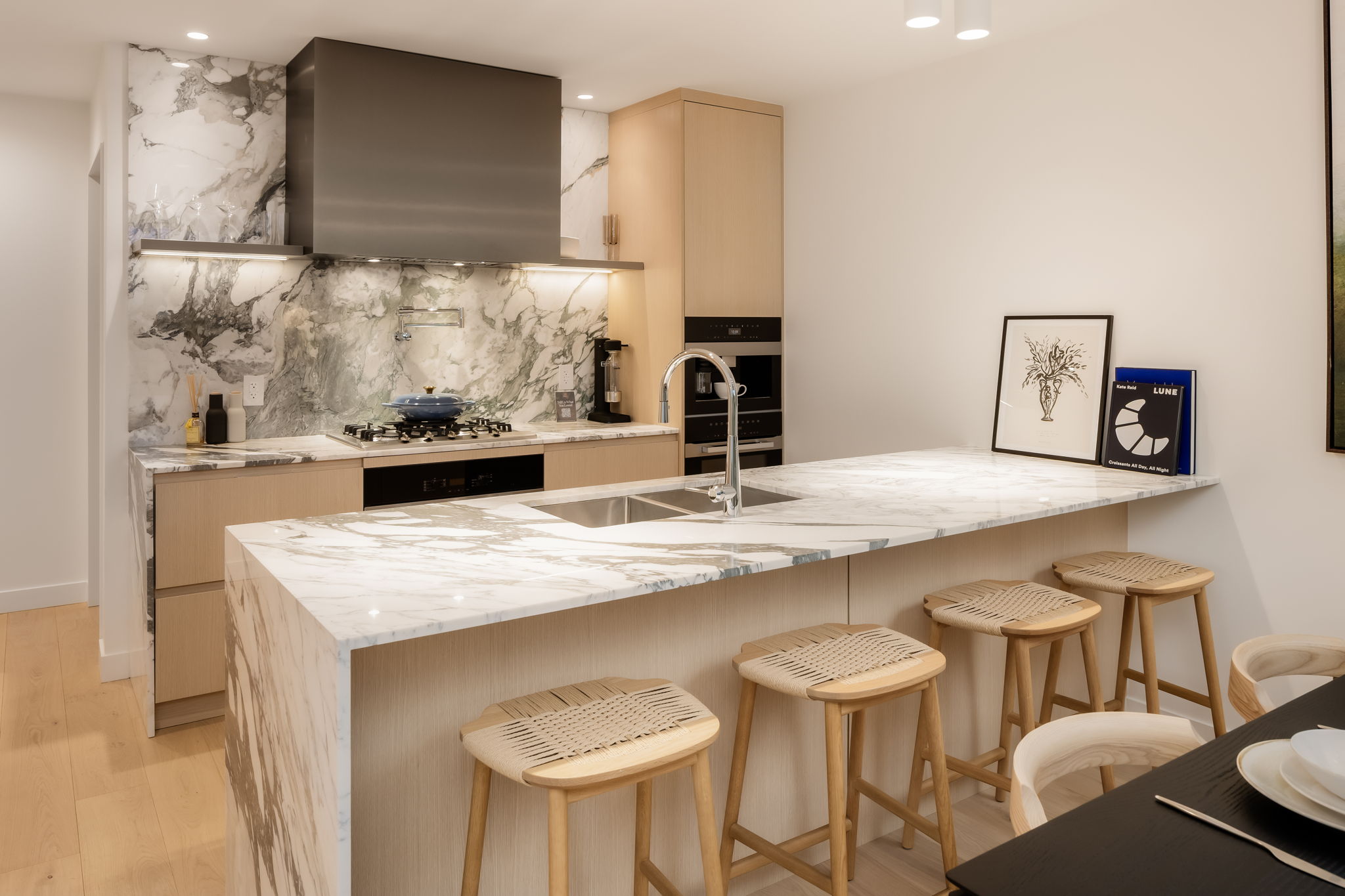 Modern kitchen with marble waterfall island, gas cooktop, integrated hood fan, and warm wood cabinetry.